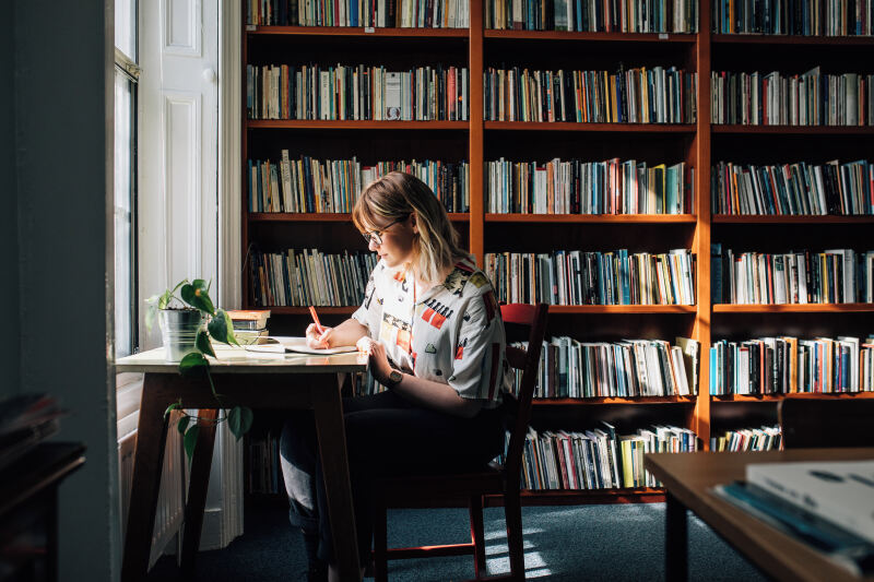 Female student at desk against a bookcase backdrop